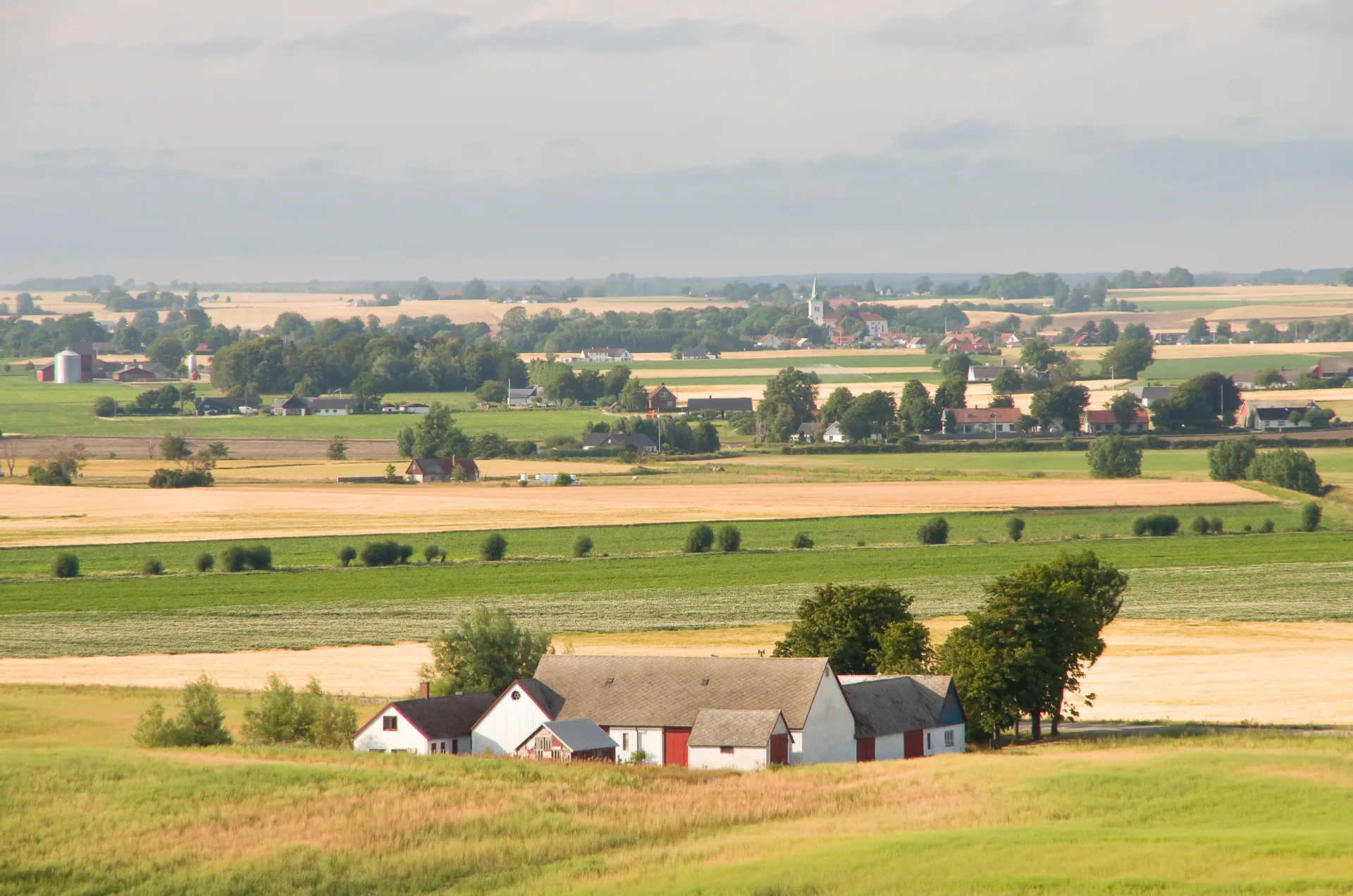Skånskt jordbrukslandskap med gård, åkrar och by i bakgrunden
